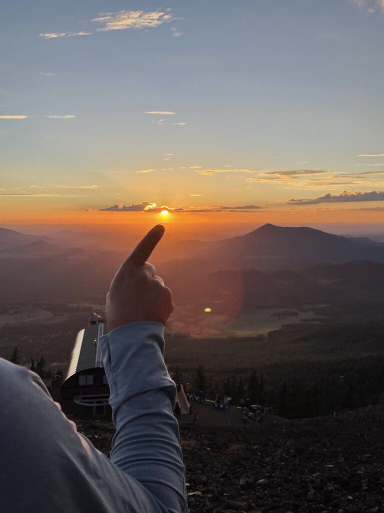 A finger pointing to the sun as it sets, cropped