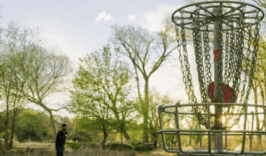 A person standing in front of trees and a metal object.