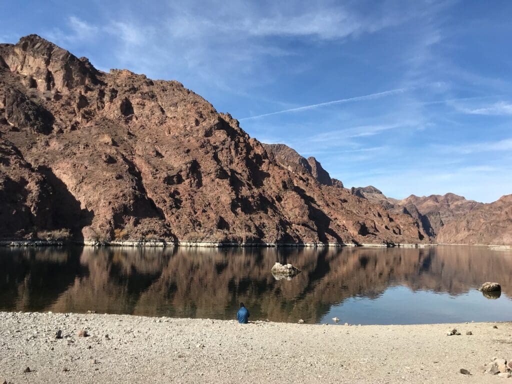 A lake with mountains in the background and a person sitting on it.