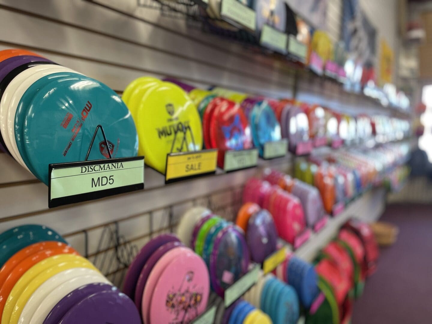 Colorful disc golf discs displayed on a retail store wall, with a focus on a blue disc labeled "discmania md5.